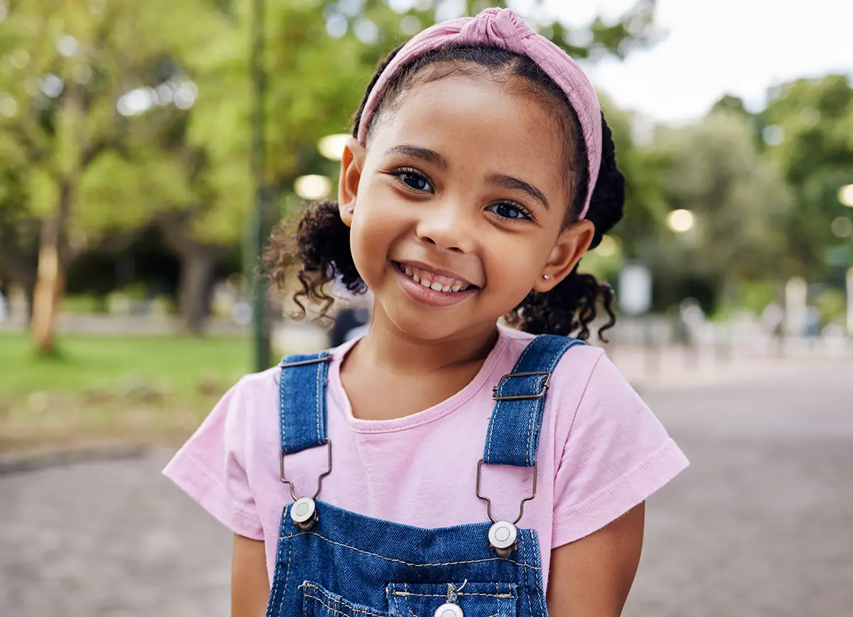 a smiling little girl in overalls at the park