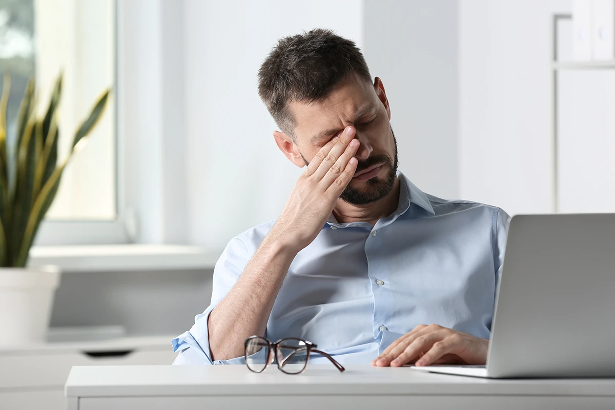 a man sitting at his desk rubbing his eye