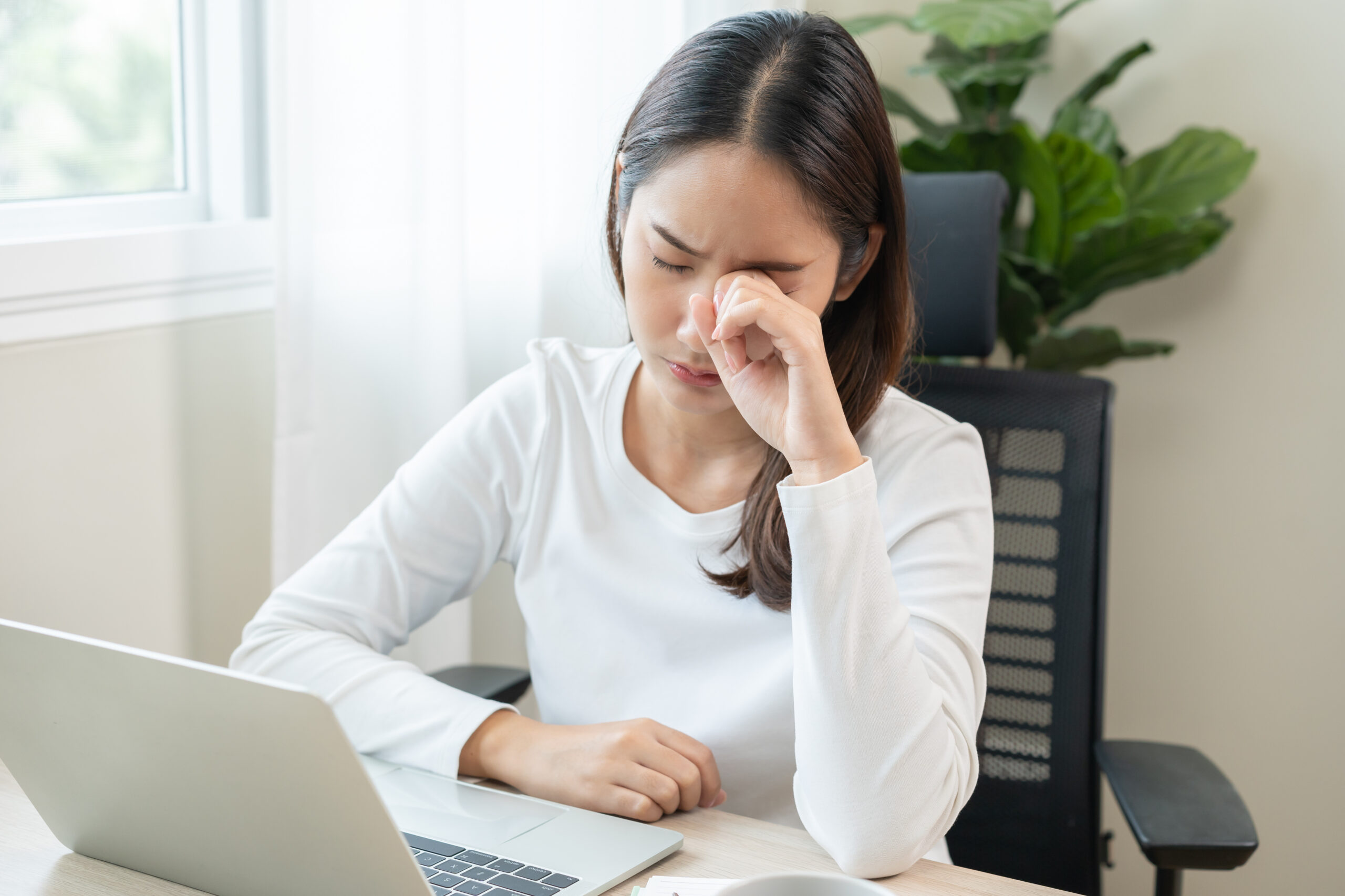 A young woman sitting at a computer rubs her dry tired eyes.