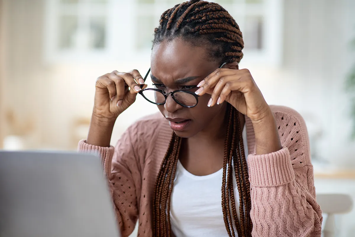 a woman squinting while looking at a laptop with glasses on